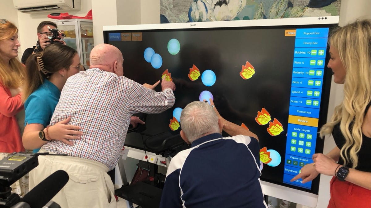 Two residents at Garden Village, along with caregivers, take part in interactive games on the SMART Board.