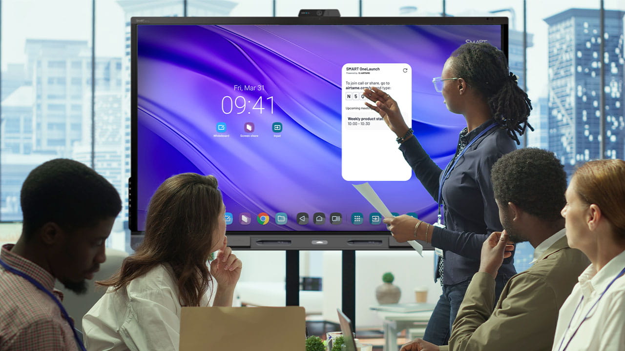 A woman points to the SMART OneLaunch widget on a QX Pro interactive display during a business meeting.