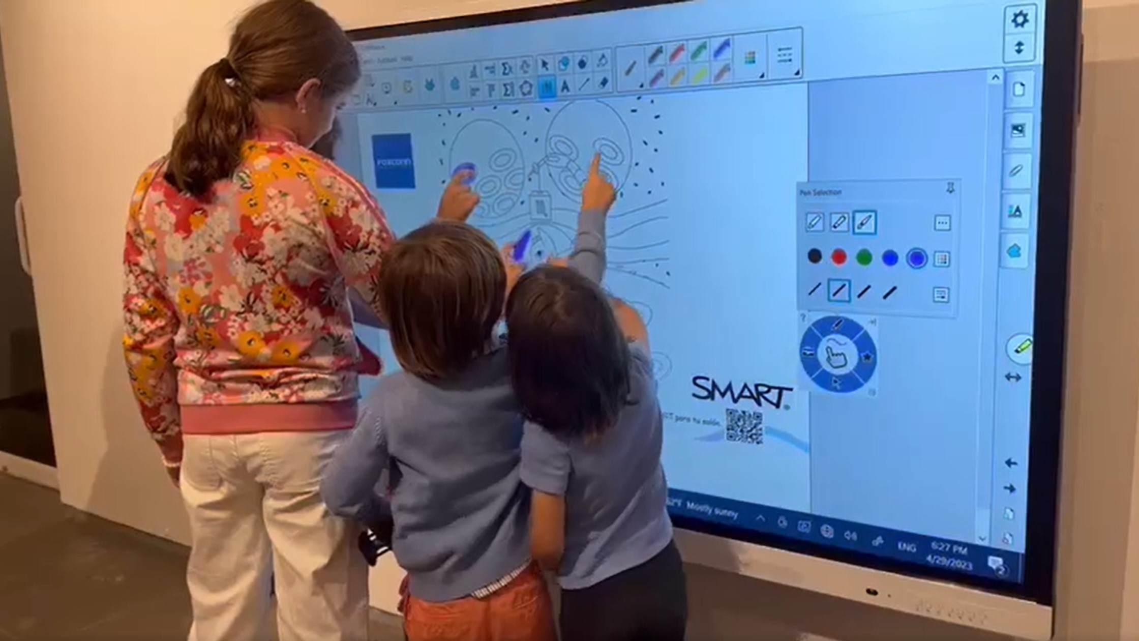Un adulto y tres estudiantes interactúan con el tablero SMART al mismo tiempo para crear una Mandala digital.