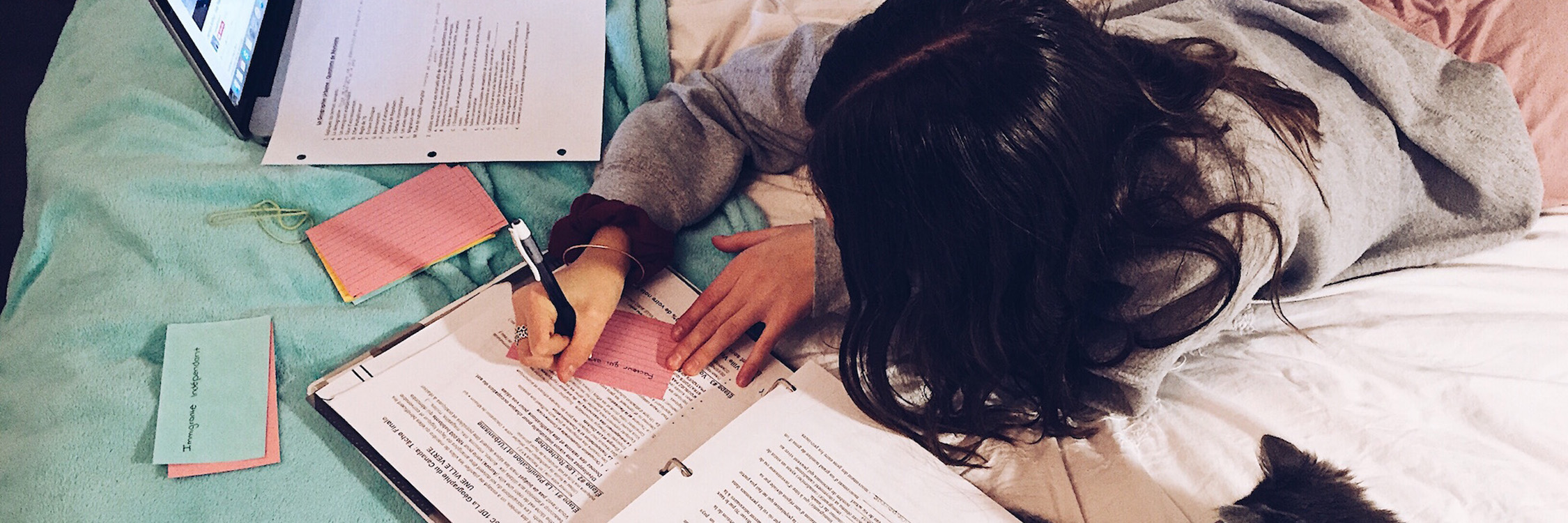 A student working independently on homework on a bed.