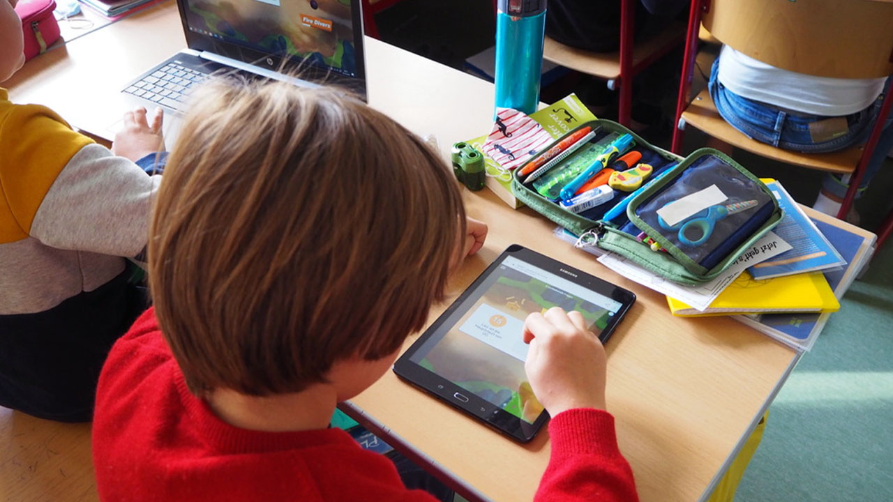 Student working on a tablet while seated at a classroom desk.