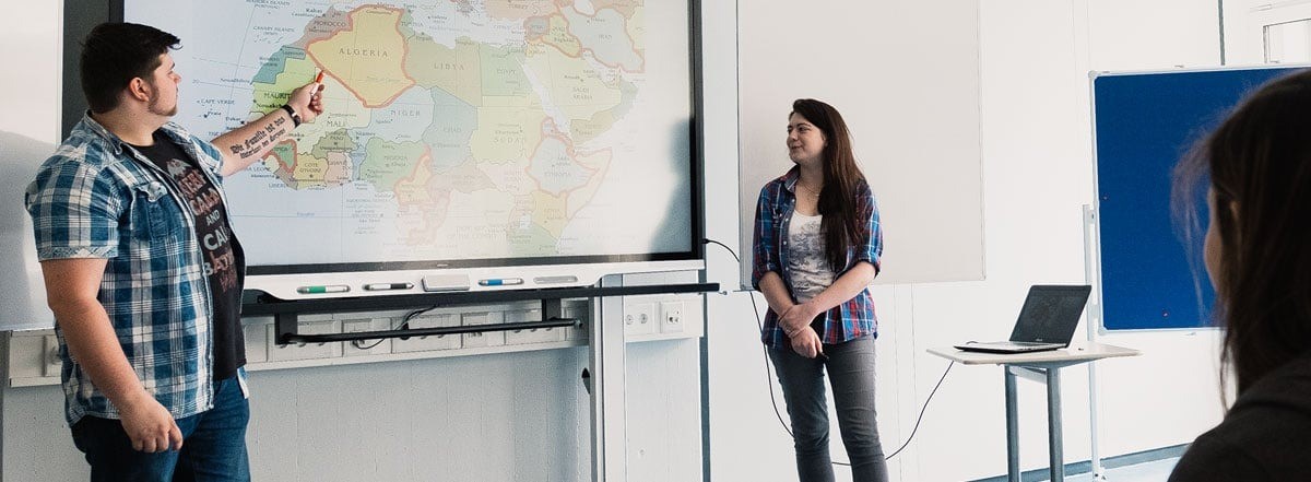 Classroom session featuring students presenting a map on a SMART Board interactive display.