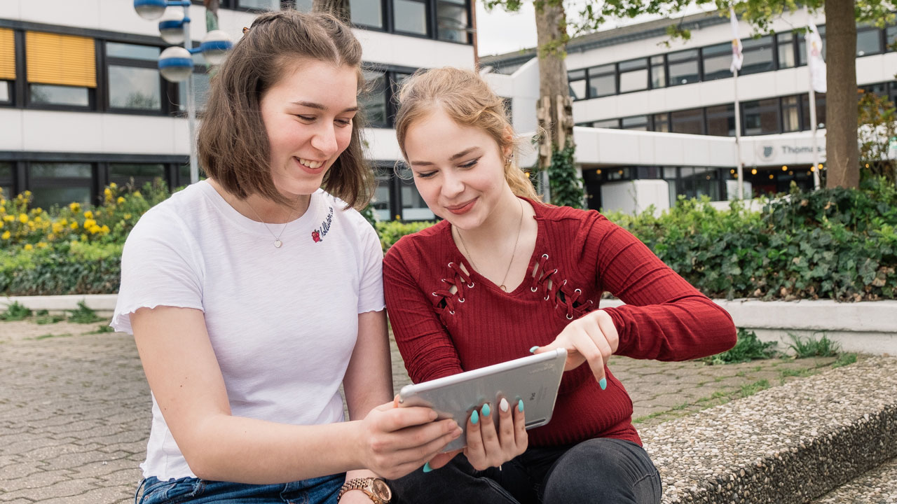 Two students collaborating on a tablet outside their school building.
