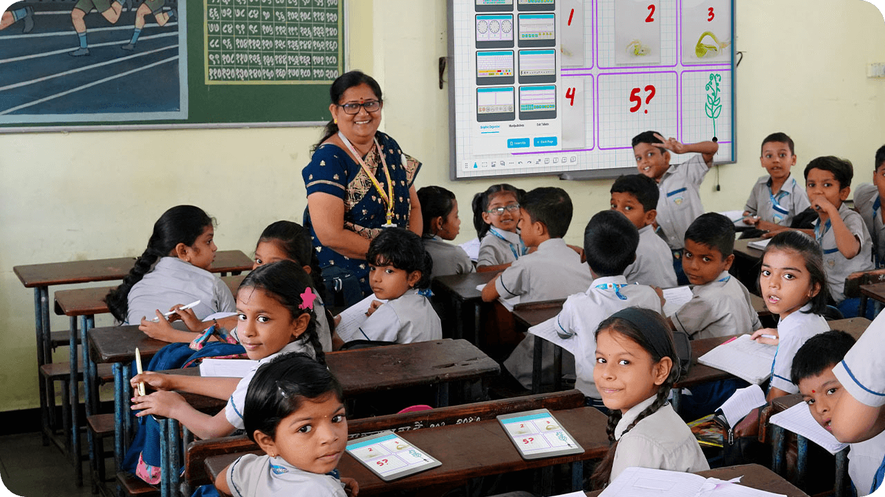 Teacher and students in a classroom, engaging in a lesson with a SMART interactive display and individual devices on desks.