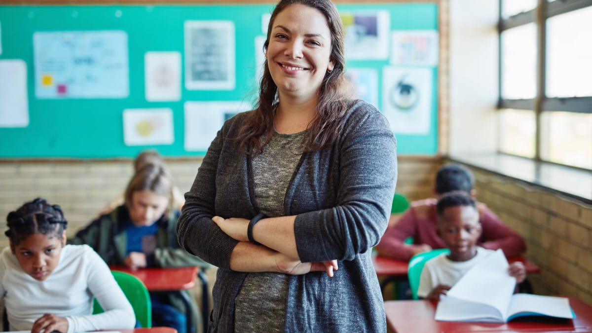 A teacher stands at the front of the classroom with her students working independently behind her.