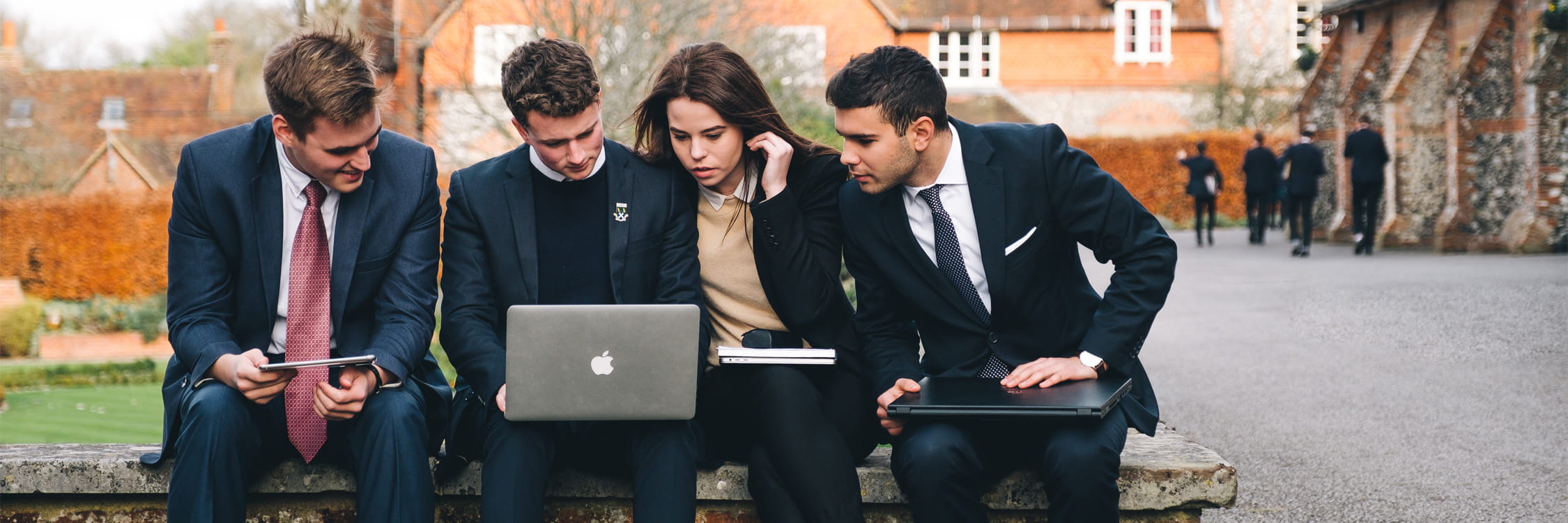 Four older students engaged on one student device.