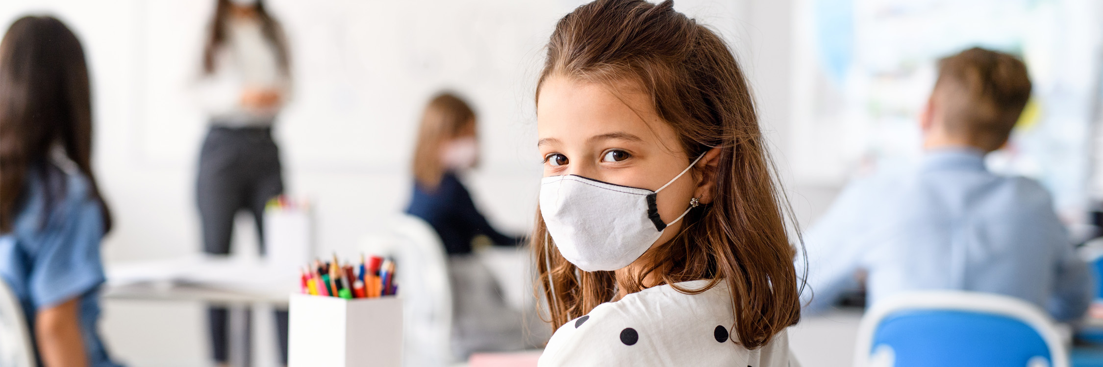 Female student in a classroom, wearing a mask.