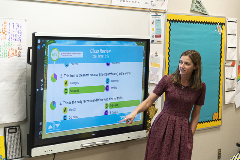 Educator pointing at a multiple-choice quiz on a SMART Board in a classroom setting.