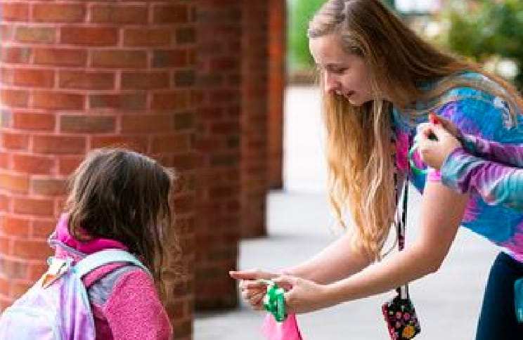 School staff greeting a student at the entrance for an event called "Awesome Kid Day".