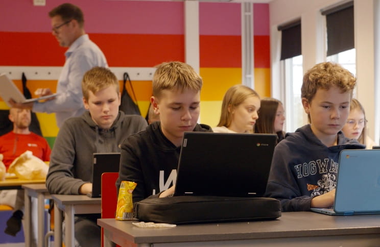 Middle school students working on laptops in a colorful classroom.