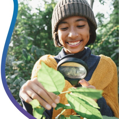 Young boy examining a leaf with a magnifying glass outdoors.