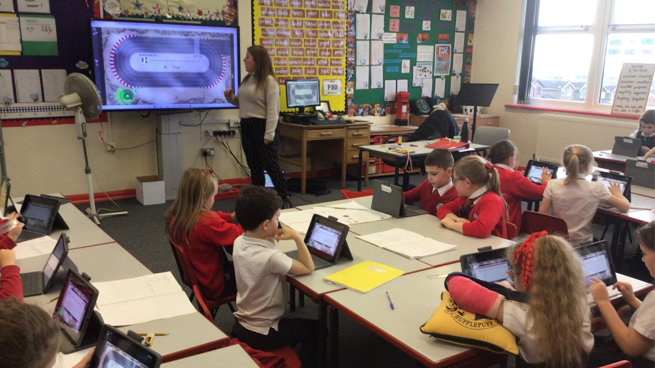 Alt text: A classroom at Sandford Hill Primary School showcasing students working on their student devices and a teacher instructing on her SMART Board.